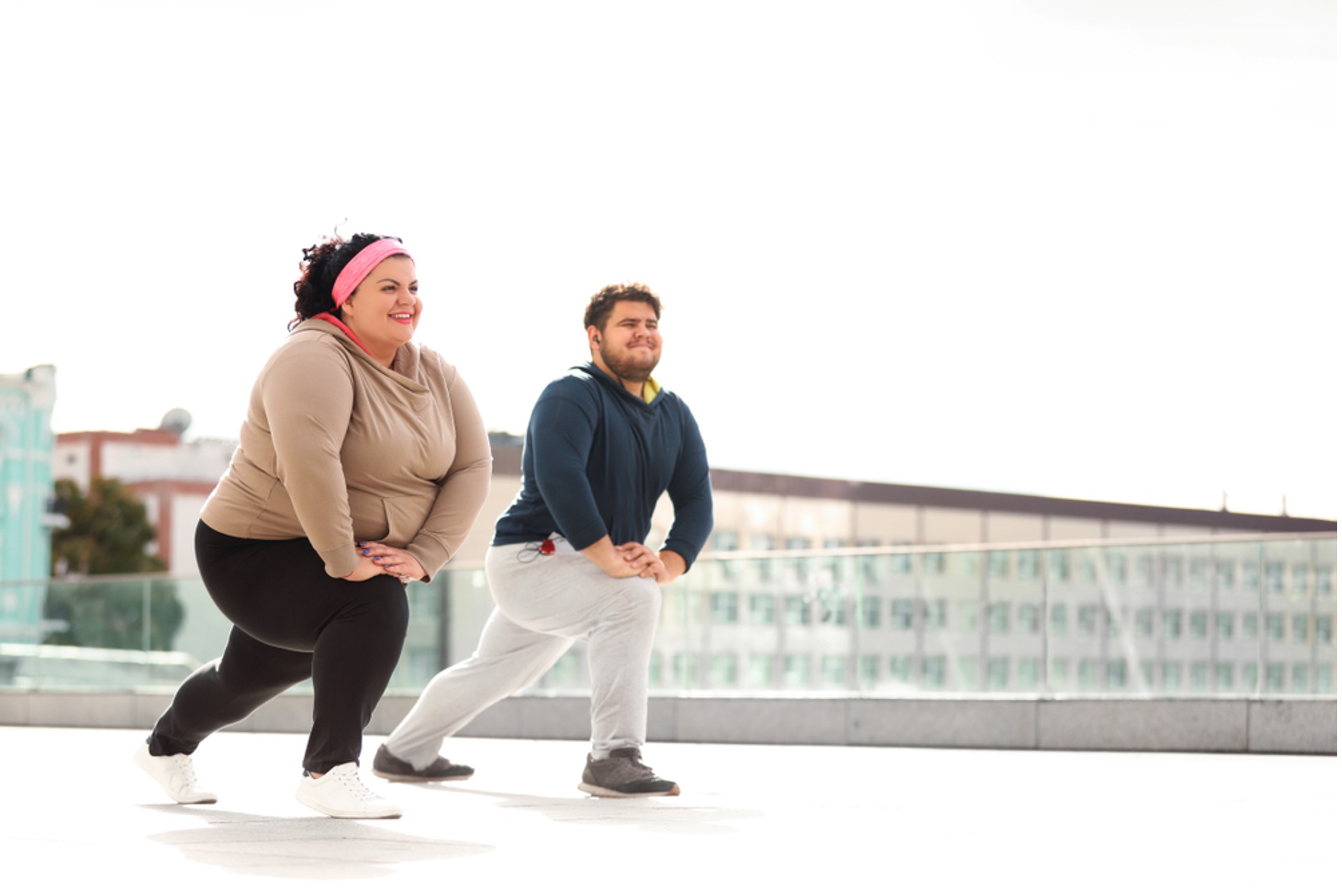 A man and woman happily doing lunge exercises together outside as a part of their weight loss journey.