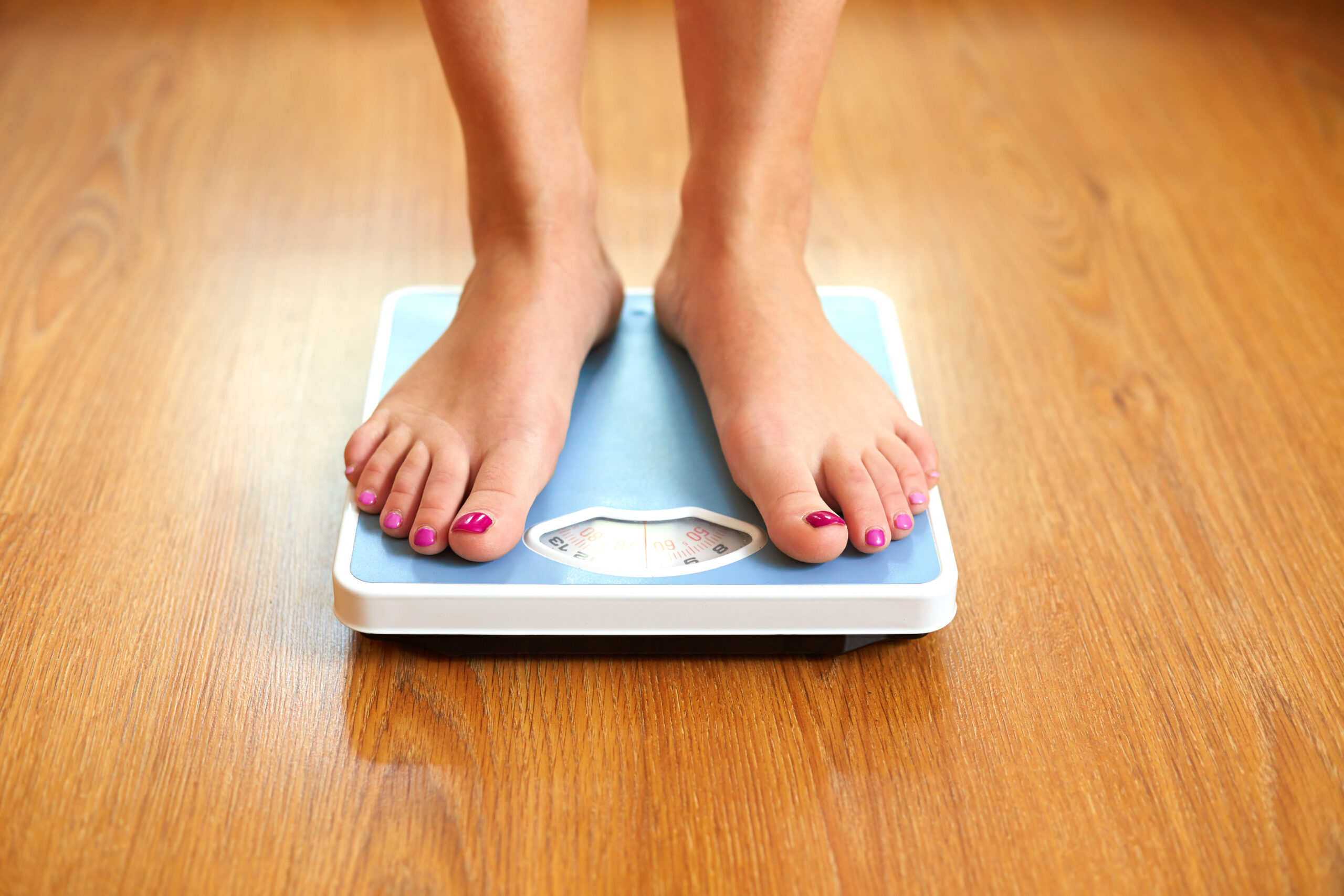 Woman standing on blue  weight scale to measure her weight loss goals.