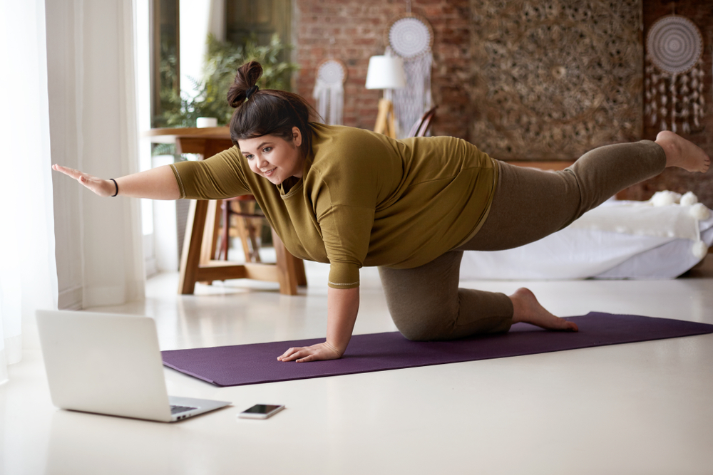 Woman dressed in brown trying to lose weight and lower cholesterol by doing yoga while looking at her computer.