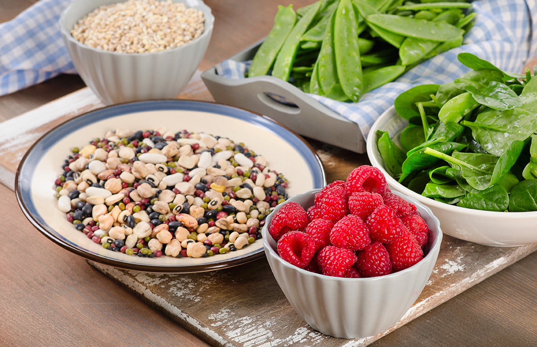 Bowls of beans, berries, spinach, and other healthy fiber-rich foods good for weight loss sit on a table