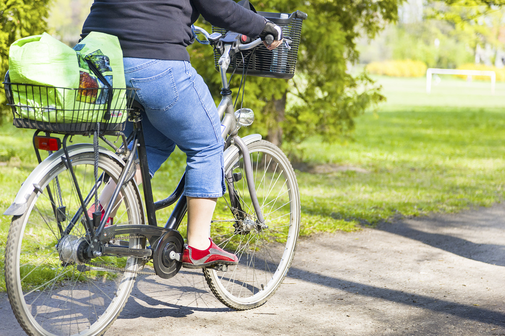 A person wearing red shoes, jeans, and a black top rides their bike on a path through a park.